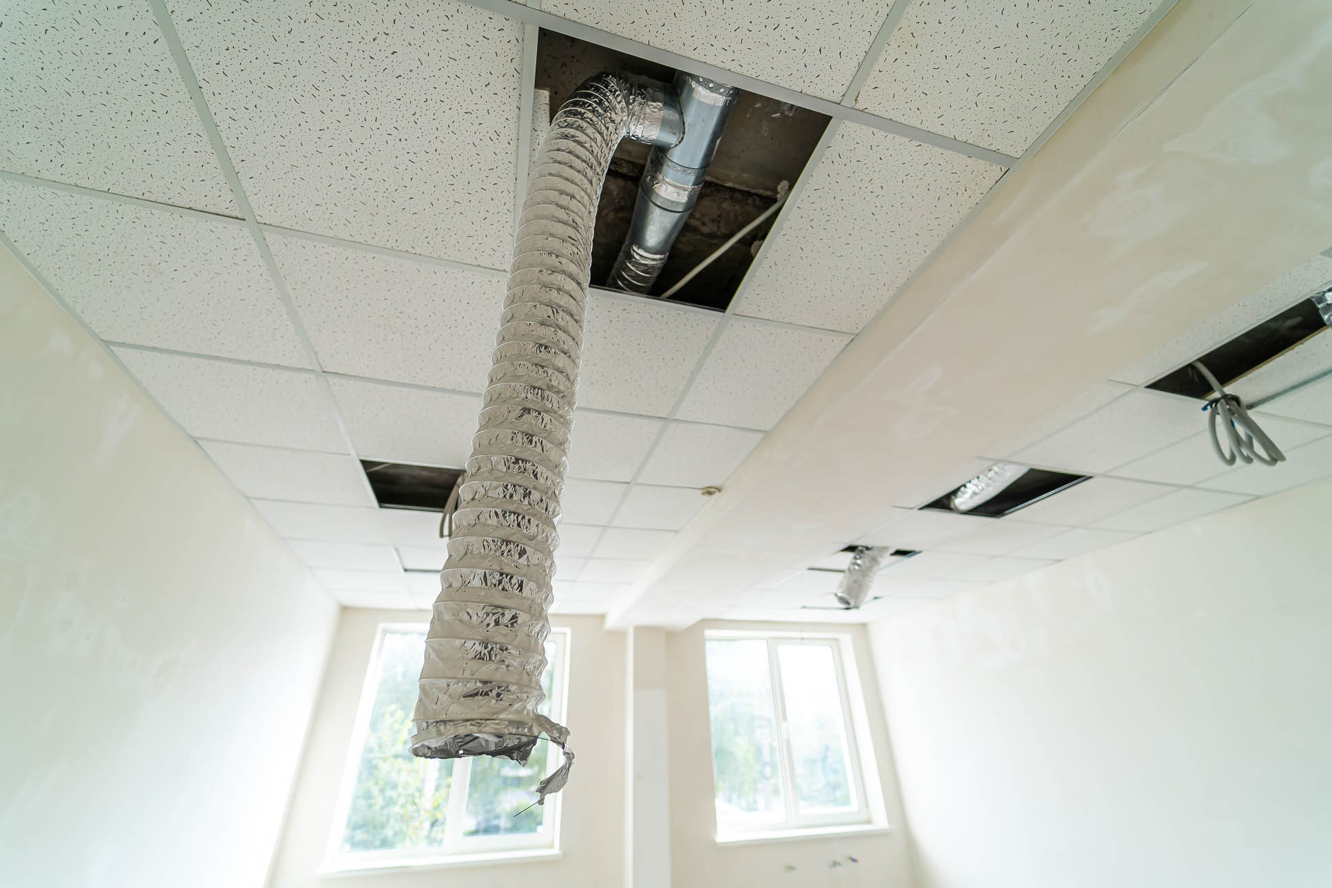 Ceiling repair in a room showing exposed ductwork and light fixtures. A room undergoing maintenance with exposed ductwork and lights revealing the ceiling’s interior